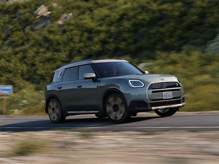 Повністю електричний MINI Countryman в кольорі Smokey Green і з яскравим сріблястим дахом - вигляд збоку.