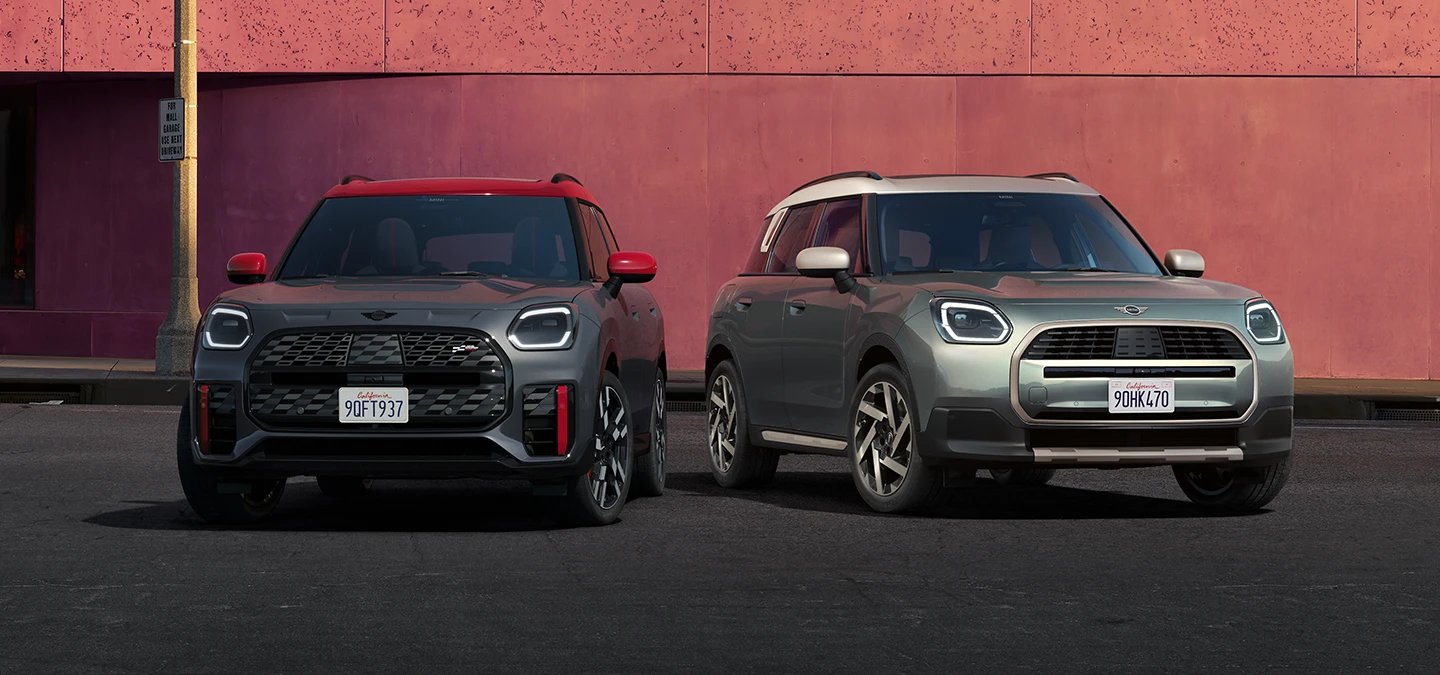 Вид спереду на MINI Countryman John Cooper Works ALL4 кольору Legend Grey з червоним дахом і MINI Countryman кольору Smoky Green з яскравим сріблястим дахом.